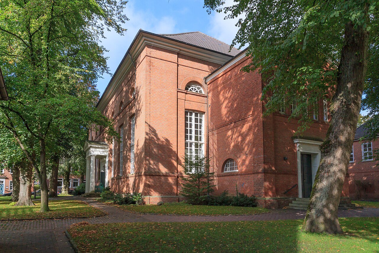 Die klassizistische Lambertikirche aus rotem Backstein zwischen Bäumen in der Auricher Altstadt