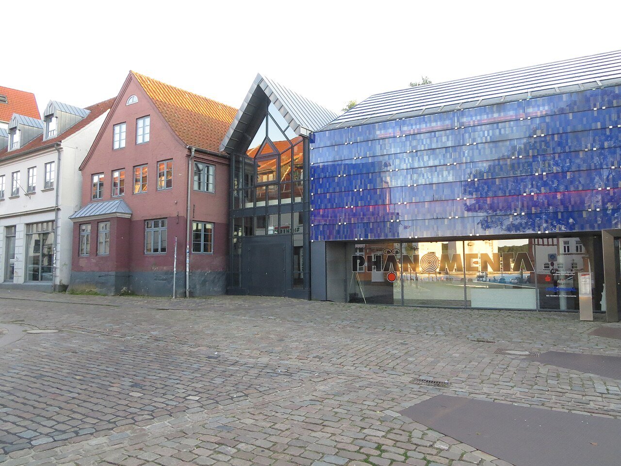 Blau schimmernde Fassade der Phänomenta Flensburg mit großem Schriftzug hinter der Glasfront