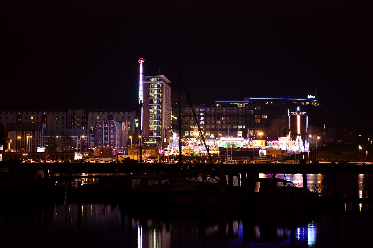Festlich beleuchteter Rostocker Weihnachtsmarkt mit Riesenrad und Lichtern, die sich abends im Wasser der Warnow spiegeln.