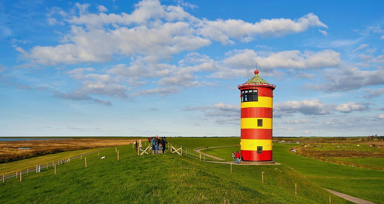 Der gelb-rot gestreifte Pilsumer Leuchtturm auf dem grünen Deich an der ostfriesischen Nordseeküste